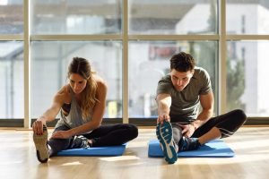 mann und frau dehnen beine auf matte in fitnesstudio